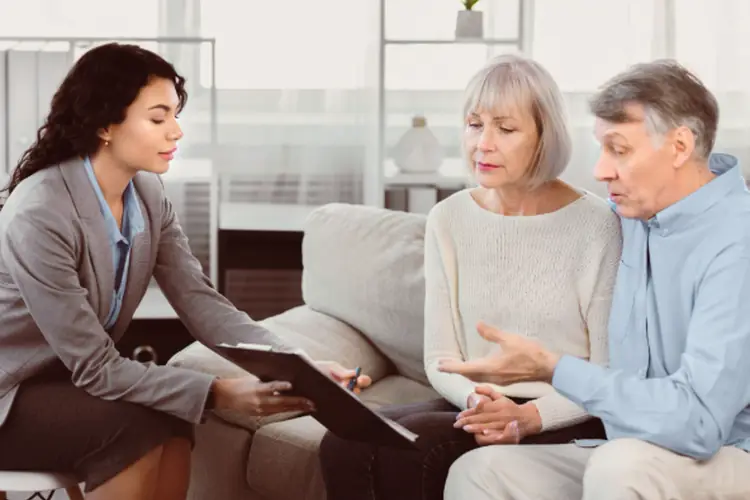 Mature man sitting on couch, embracing wife, signing papers with consultant.
