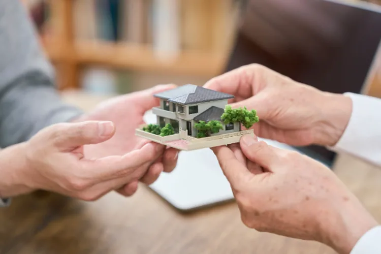 Two people holding a home model symbolizing a transfer of inheritance. 